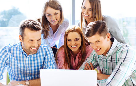 Gruppe junger Menschen zwei Männer und drei Frauen schauen lachend gemeinsam auf einen Laptop